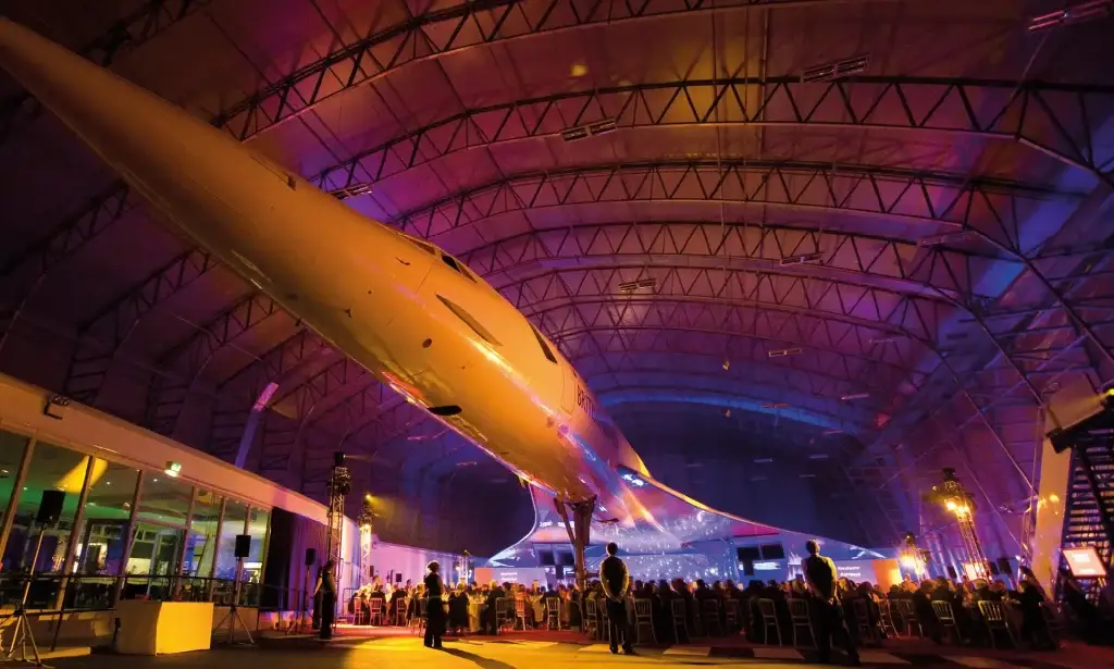 An image of an award ceremony taking place in a hangar with a large plane in the middle of it